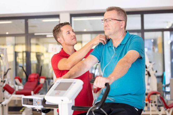 Physiotherapeut betreut älteren Mann mit Sauerstoffnasebrille beim Ergometertraining