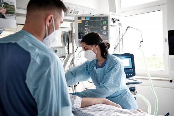 Zwei Personen in Schutzkleidung versorgen Patient im Krankenhaus an Monitoren im Intensivzimmer