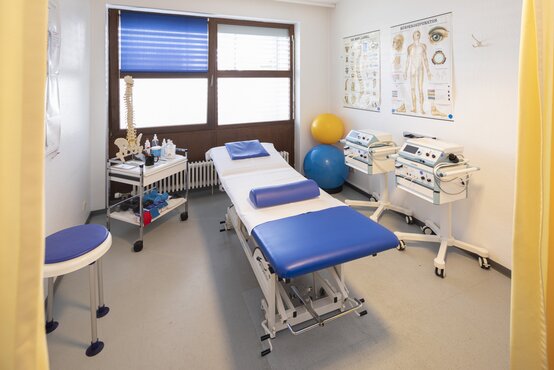 Heller Physiotherapieraum der Schön Klinik Lorsch mit blauer Liege, Gymnastikbällen, medizinischen Geräten und Anatomie-Poster