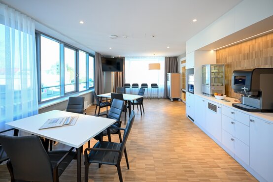 Heller, moderner Aufenthaltsraum der Schön Klinik Lorsch mit Sitzgruppe, Küchenzeile, Kaffeeautomat und großen Fenstern