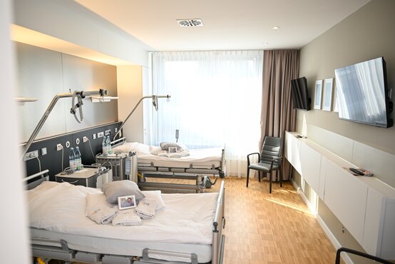 Modernes Patientenzimmer der Schön Klinik Lorsch mit zwei Betten, Holzboden, großem Fenster und neutraler Einrichtung