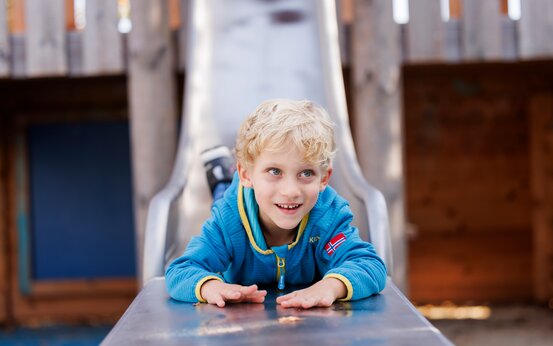 Blondes Kind rutscht vorwärts auf dem Bauch Rutsche auf Klinikspielplatz runter