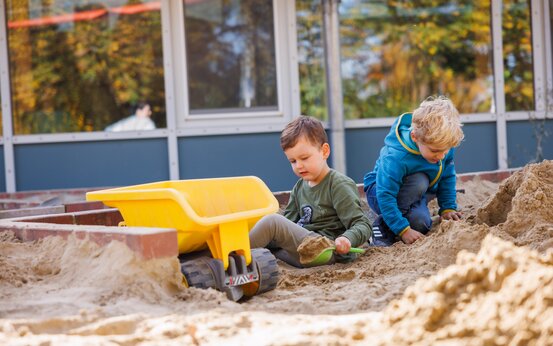 Zwei Kinder spielen mit Schaufel und Händen im Sandkasten auf Klinikspielplatz
