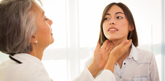 Ärztin tastet den Hals einer Patientin zur Untersuchung einer Schilddrüsenvergrößerung