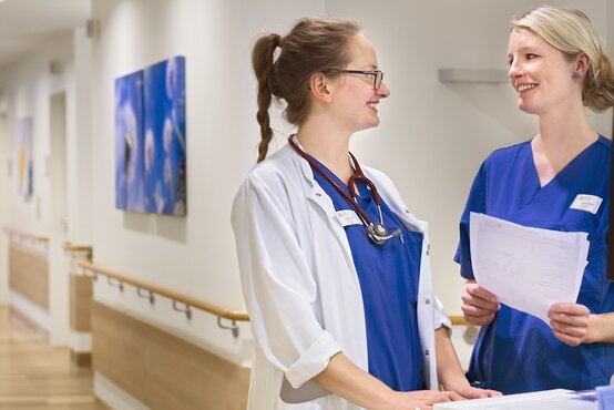 Ärztin im weißen Kittel und Pflegekraft besprechen Patientendaten am Computer im Krankenhausflur.