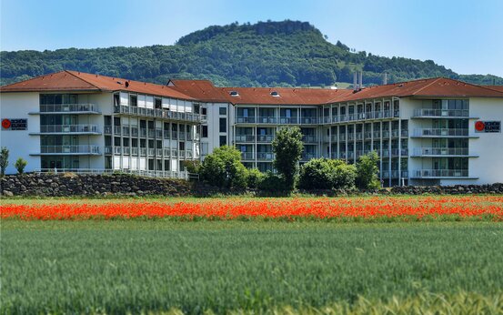 Modernes Hauptgebäude der Schön Klinik Bad Staffelstein im Grünen, umgeben von blühenden Wiesen, Feldern und Hügeln