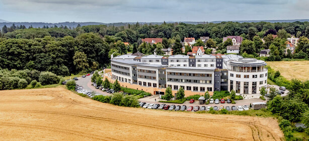 Großer, moderner Klinikkomplex der Schön Klinik Bad Arolsen, Parkplatz, Feld und Wald im Hintergrund