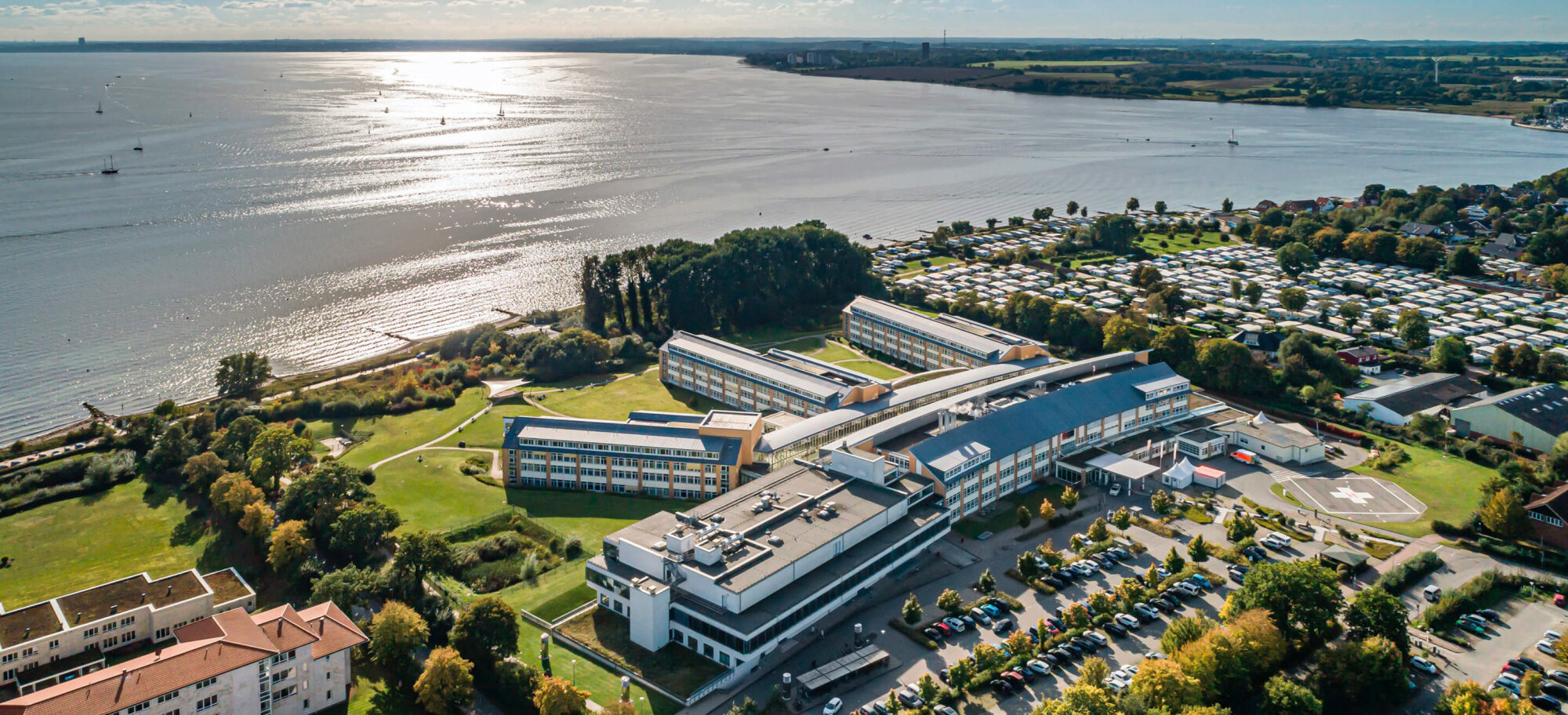 Luftaufnahme der Schön Klinik Neustadt an der Küste mit Klinikgebäuden, Parkplätzen und umliegender Natur