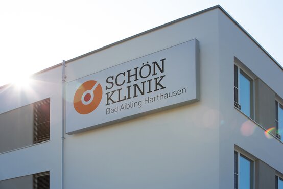 Moderne Fassade der Schön Klinik Bad Aibling Harthausen mit großem Schild und Sonnenschein