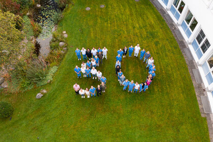 Großes Gruppenfoto von Klinikmitarbeitern, die auf einer Wiese die Zahl „30“ zum Jubiläum formen