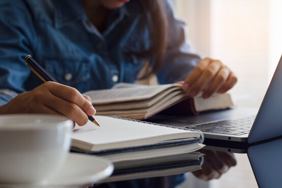 Auszubildende lernt am Schreibtisch mit Notizbuch, Buch und Laptop