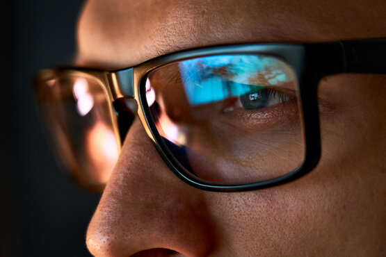 Nahaufnahme von Augen hinter schwarzer Brille mit Monitor-Reflexion