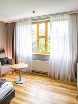 Helles, modernes Einzelzimmer mit großem Fenster, Einzelbett, Sessel, Schreibtisch und freundlicher Atmosphäre