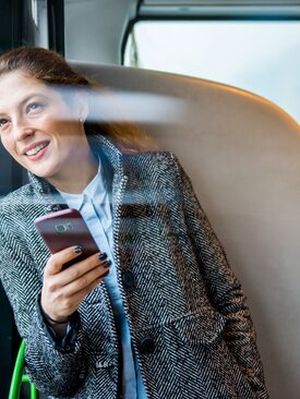 Junge Frau mit Smartphone im Bus, schaut aus dem Fenster