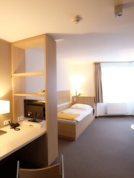 Modern eingerichtetes Einzelzimmer in der Schön Klinik mit Bett, Schreibtisch, Sesseln und Tageslicht