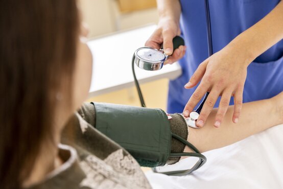 Medizinisches Fachpersonal misst Blutdruck einer Patientin mit Manschette und Stethoskop