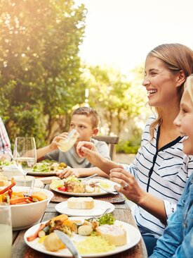 Glückliche Familie mit zwei Kindern isst gemeinsam gesunde Mahlzeit mit Salat und Brot an Holztisch