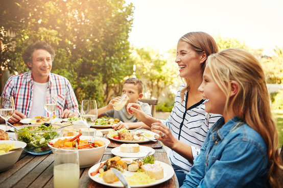 Glückliche Familie mit zwei Kindern isst gemeinsam gesunde Mahlzeit mit Salat und Brot an Holztisch