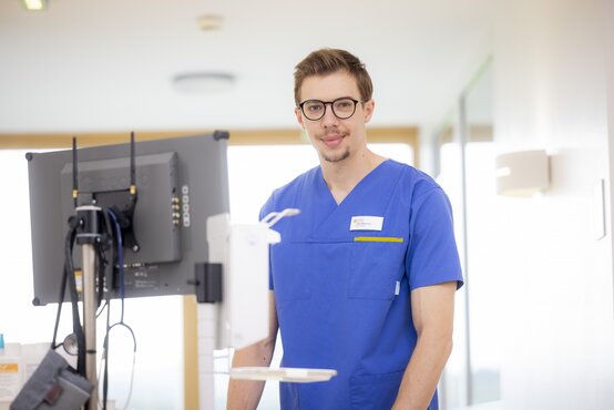 Junger Pfleger in blauer Kleidung dokumentiert am Computer auf Krankenhausstation