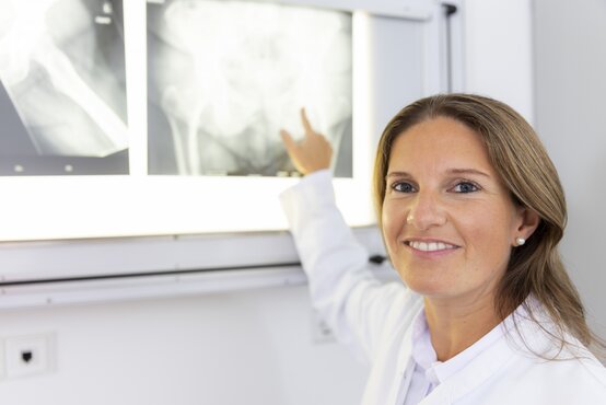 Ärztin im weißen Kittel zeigt lächelnd auf ein Röntgenbild in moderner Praxis, medizinische Diagnostik