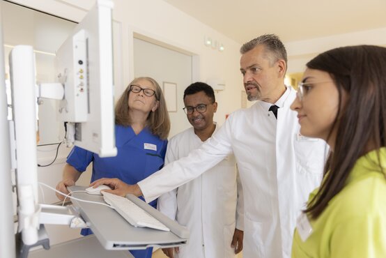 Vier medizinische Fachkräfte bei digitaler Visite am Computer in heller Klinik