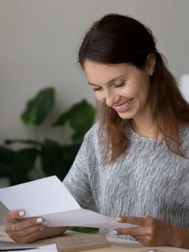 Junge Frau mit braunen Haaren liest lächelnd einen Brief
