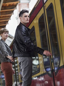 Junge Frau und Mann steigen am Bahnhof in gelb-rote Bahn ein, Spiegelung und Fahrradsymbol im Fenster sichtbar