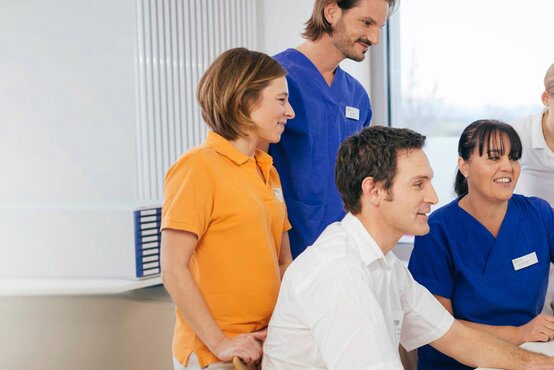 Fünf medizinische Fachkräfte im Krankenhausbüro schauen gemeinsam auf einen Computerbildschirm