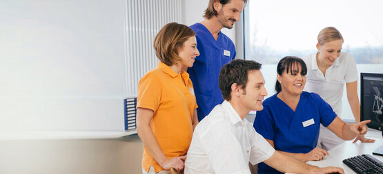 Fünf medizinische Fachkräfte im Krankenhausbüro schauen gemeinsam auf einen Computerbildschirm