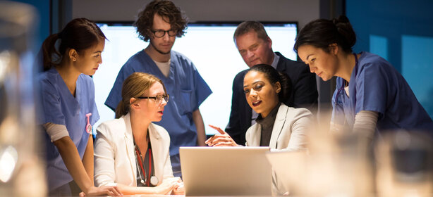 Interdisziplinäres Team aus Ärzt:innen und Fachkräften arbeitet gemeinsam an einem Laptop