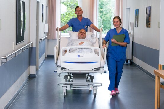 Krankenhauspersonal schiebt einen liegenden Patienten im Bett durch einen hellen Krankenhausflur