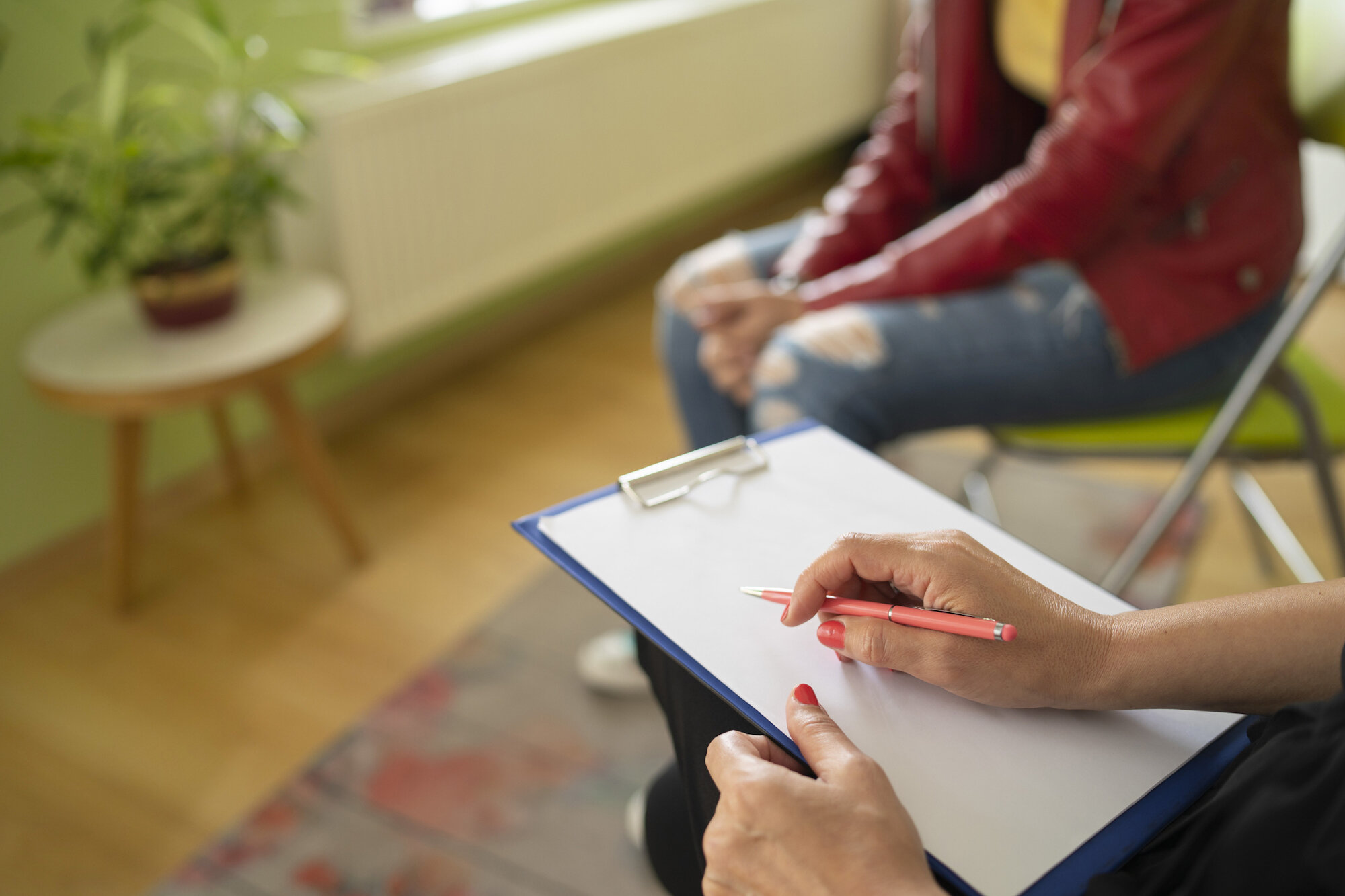 Therapeutin mit Klemmbrett und Stift bei Psychotherapie-Sitzung, Patientin sitzt gegenüber
