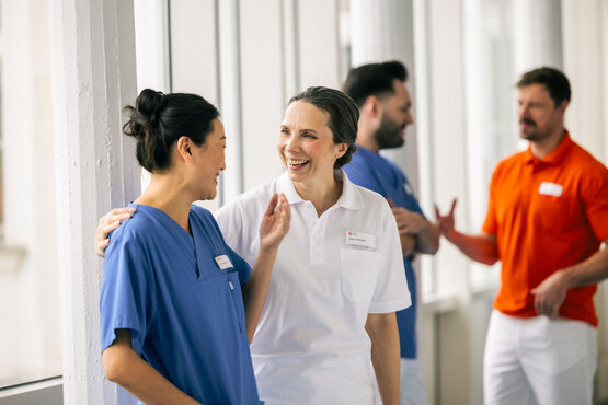 Vier Mitarbeitende der Schön Klinik Gruppe im Gespräch auf einem modernen Klinikflur, zwei in blauer, zwei in weißer Kleidung.