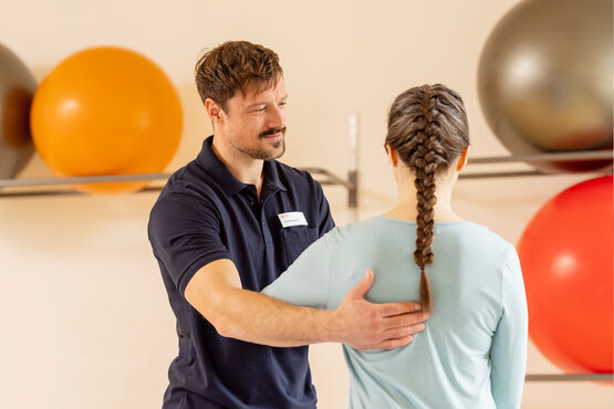 Therapeut unterstützt Patientin bei einer Übung in heller Praxis mit bunten Gymnastikbällen.