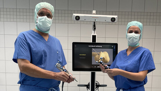 Zwei Chirurgen in blauer OP-Kleidung bedienen Navigationssystem mit Gelenksimulation im OP-Saal