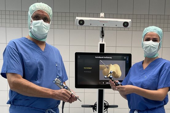 Zwei Chirurgen in blauer OP-Kleidung bedienen Navigationssystem mit Gelenksimulation im OP-Saal