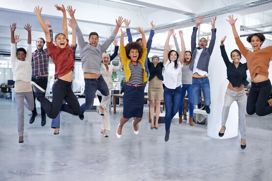 Vielseitiges Team springt gemeinsam lachend im modernen Büro
