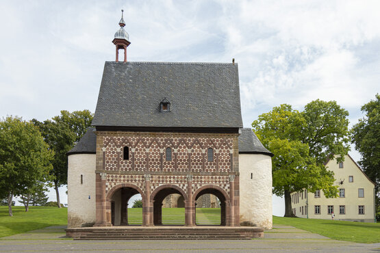 Historisches Gebäude mit Rundbögen, gemustertem Mauerwerk und Türmen im Klosterpark Lorsch