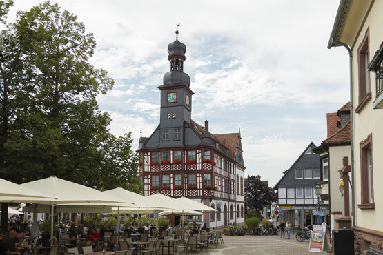 Historischer Marktplatz in Lorsch mit Fachwerk-Rathaus, Uhrturm, Außengastronomie, Sonnenschirmen, Bäumen und Fachwerkhäusern
