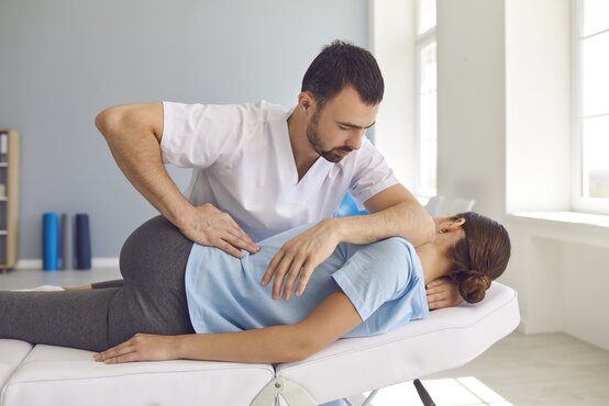 Physiotherapeut führt manuelle Therapie am Rücken einer seitlich liegenden Frau auf Behandlungsliege im hellen Therapieraum durch