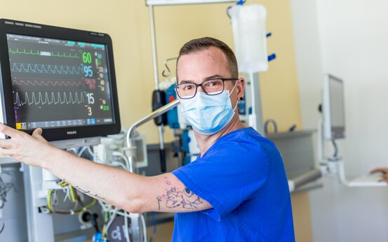 Krankenpfleger in blauer Dienstkleidung mit Mundschutz überwacht Vitalwerte am Monitor