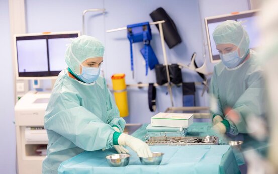 Medizinisches Personal in OP-Kleidung bereitet chirurgische Instrumente auf blauem Tuch im Operationssaal vor