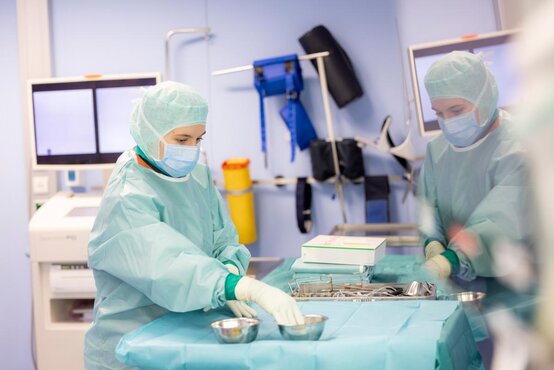 Medizinisches Personal in OP-Kleidung bereitet chirurgische Instrumente auf blauem Tuch im Operationssaal vor