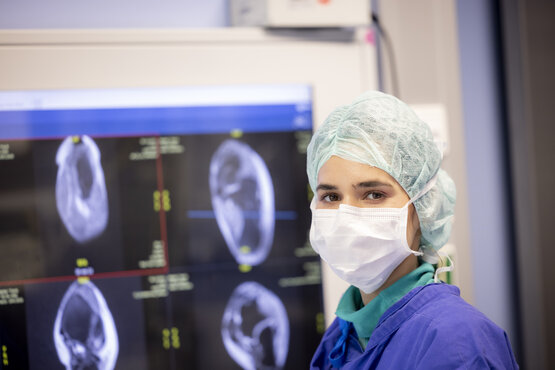 Medizinische Fachkraft mit Schutzkleidung und Mund-Nasen-Schutz vor Monitor mit MRT-Aufnahmen im Krankenhaus