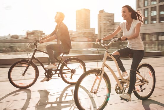 Zwei junge Erwachsene fahren bei Sonnenschein auf Fahrrädern durch eine moderne Stadt, genießen den Tag und die urbane Landschaft