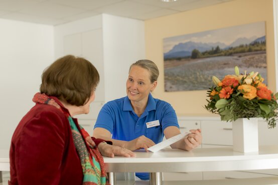 Freundliche Beratung in der Tagesklinik für Demenz München: Zwei Frauen am weißen Tisch mit Blumenstrauß