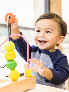 Kind übt beidhändig Feinmotorik an farbigem Holz-Motorikspielzeug mit Drahtschlaufen im hellen Ergotherapie-Raum der Klinik