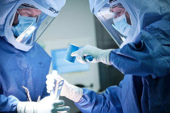 Zwei Chirurgen in OP-Kleidung und Gesichtsschutz führen gemeinsam eine Operation im sterilen Operationssaal durch
