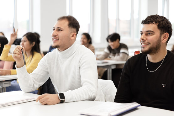 Schüler in der Weiterbildung der Schön Klinik im hellen Seminarraum, eine Person hebt fragend die Hand.