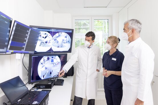 Drei medizinische Fachkräfte mit Mundschutz besprechen Überwachungsbilder an Monitoren auf Komplexstation der Schön Klinik Roseneck